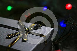 Defocus gray gift with close-up gold bow ribbon on pine or fir tree blurred background with glowing festive green and