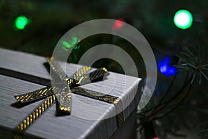 Defocus gray gift with close-up gold bow ribbon on pine or fir tree blurred background with glowing festive green, red