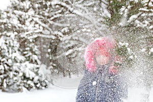 Defocus little funny girl in red warm hat shakes the snow from a branch outside on nature winter snowy forest background