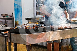 Defocus man cooking bbq meat at festival outdoor. Seafood paella. Chef grilling sausages in park outside. Concept of