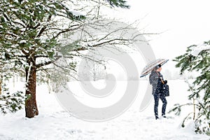 Defocus man standing or walking in snowy pine forest in winter and holding umbrella. Winter snowy woodland. Natural pine