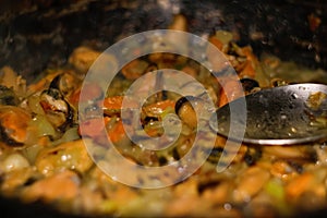 Defocus mussels dish on pan. Delicious seafood mussels with parrot and onion. Heap of peeled mussels with spoon close-up