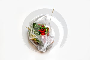 DEFOCUS. Plastic nature. Red and green plants flowers in a plastic bag on a white background. A dry blade of grass