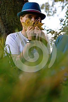 Defocus portrait of a funny young woman with brown hair wearing a hat outdoors. Female hand holding yellow dry leaves