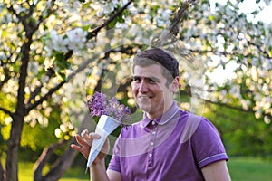 Defocus portrait of handsome smiling caucasian man with cone flowers in lilac garden. Funny young brunette guy smelling