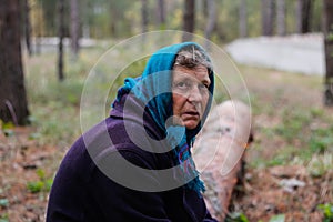 Defocus portrait of russian grandmother senior old woman seating on log in pine autumn forest. Old women in coat and