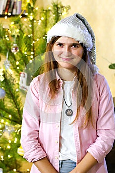 Defocus portrait of smiling youth brunet woman 20-25 years wearing white santa hat and pink shirt. Posing indoor with