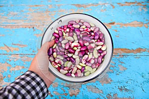 Defocus purple beans background. Hand holding plate on blue background of many grains of dried beans. Brown beans