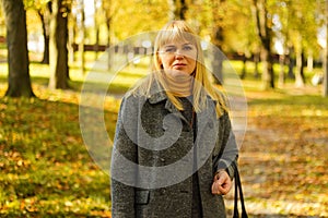 Defocus serious blond 40s woman posing in yellow autumn park. Happy beautiful lady. Women wearing grey pullover, yellow