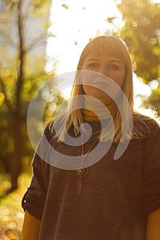 Defocus serious blond 40s woman standing in yellow autumn park. Happy beautiful lady. Women wearing grey pullover