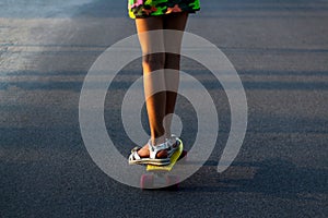 Defocus skater girl moving along asphalt road on a yellow skateboard wearing white sandals and bright dress. Street