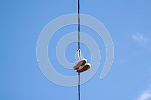 Defocus sneakers foot hanging from electrical wire against a blue sky background. The concept of urban culture, sale of