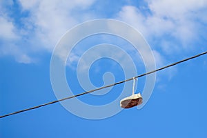 Defocus sneakers hanging from electrical wire against a blue sky background. The concept of urban culture, sale of