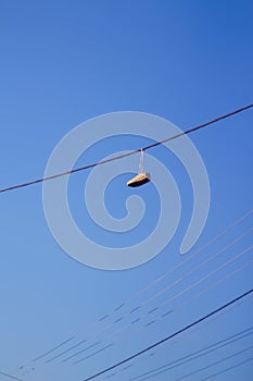 Defocus sneakers hanging from electrical wire against a blue sky background. The concept of urban culture, sale of