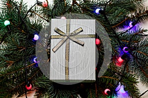 Defocus top view gray retro gift with gold bow on pine or fir tree blurred background with glowing festive light bulb