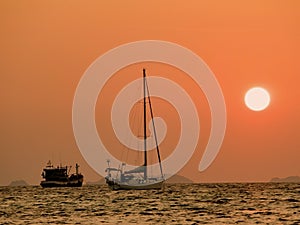 Defocus of Yachts in the sea at sunset. Silhouette boat at sunset over the sea with orange sky in background