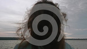 Defocused back view of brunette with long hair dancing on pier in front of water. Sky and water on background are in