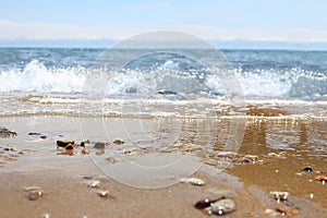 Defocused beach with blurred wave and wet sand with pebble on blue sky. Sea, ocean background. Vacation outdoor and travel holiday