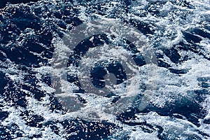 Defocused blue sea water and diagonal wave with white foam and bubbles abstract background. Selective focus