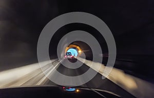 Defocused blurred road with car and blue light source at end of the tunnel.  Abstract blur motion in black gray colors. Car going