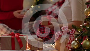 defocused couple in Christmas pajamas exchanging presents gift boxes on bed