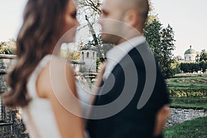 Defocused gorgeous bride and groom silhouettes on background of old castle in focus in park. Romantic moment. Stylish wedding