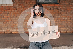 Defocused Horizontal Portrait of Woman with Poster Save Ukraine in focus. woman belligerent look