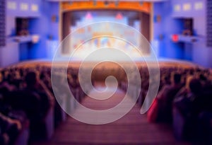 Defocused image. Auditorium in the theater during the performance. The scenery on the stage. Adults and children