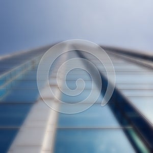 Defocused modern glass skyscraper rising up against a blue sky