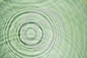 Defocused rippled transparent green water gel with concentric expanding circles on surface from fallen drop with waves