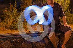 Defocused shot of man drawing blue light sign of infinity in nig