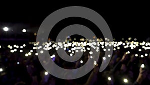 Defocused spectators in hall with lights waving in the dark. Action. Audience holding phones with shining flashlights