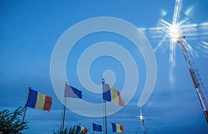 Defocused waving Romania and European Union flags waving at dusk with tall light