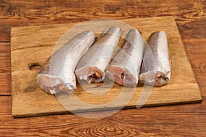 Defrosted raw Argentine hake on cutting board on rustic table