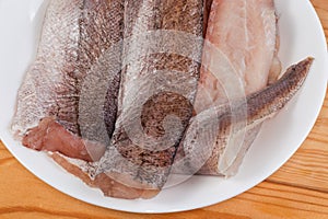 Defrosted raw hake fillets on white plate, fragment top view