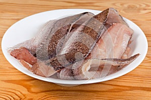 Defrosted raw hake fillets on white plate on rustic table