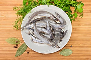 Defrosted uncooked capelin on the white dish, spice and greens