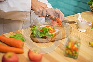 With deft professional the chef in close up shot sliced through the juicy tomato on the cutting board in a kitchen. photo