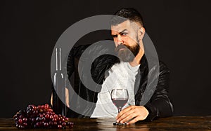 Degustator with seductive face sits by wine bottle and grapes