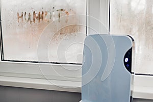 Dehumidifier with touch panel works by wet window in flat. Humidity written on window. Dampness concept photo