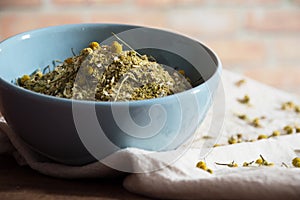 Dehydrated chamomile inside blue bowl on light background with herb flowers