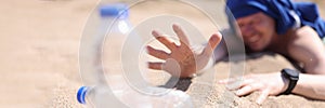 Dehydrated man crawling on sand for bottle of drinking water closeup