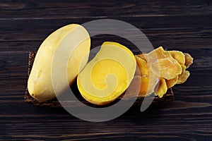 Dehydrated mango slices and fresh raw mango on wooden plate on dark background