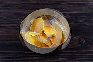 Dehydrated mango slices in a wooden bowl on dark background