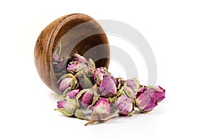 Dehydrated pink rose buds spilling from a small wooden bowl