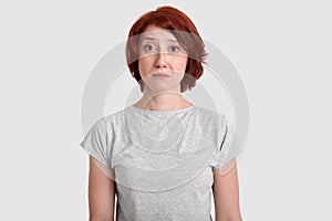 Dejected miserable woman with red hair, minimal make up, looks in displeasure at camera, wears casual grey t shirt, expresses