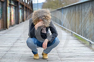 Dejected woman squatting on a bridge