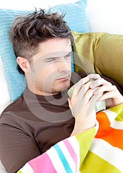 Dejected young man lying on the couch with tea