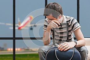 Delayed aeroplane concept. Tired passenger is sitting with baggage in airport.