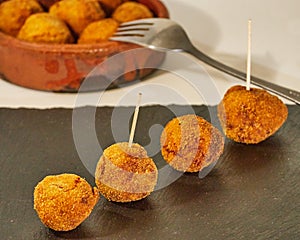 Delcious pincho of 4 round croquettes on a black slate board decorated with croquettes in a bowl of mud